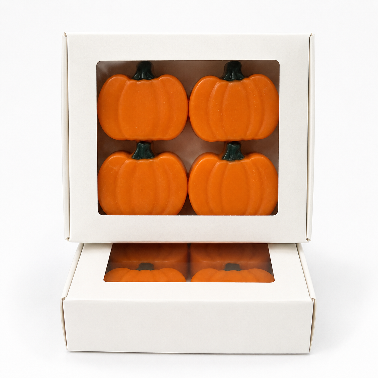Four orange pumpkin-shaped items displayed in a white gift box with a clear window, with the lid propped open and a second layer below on a white background.