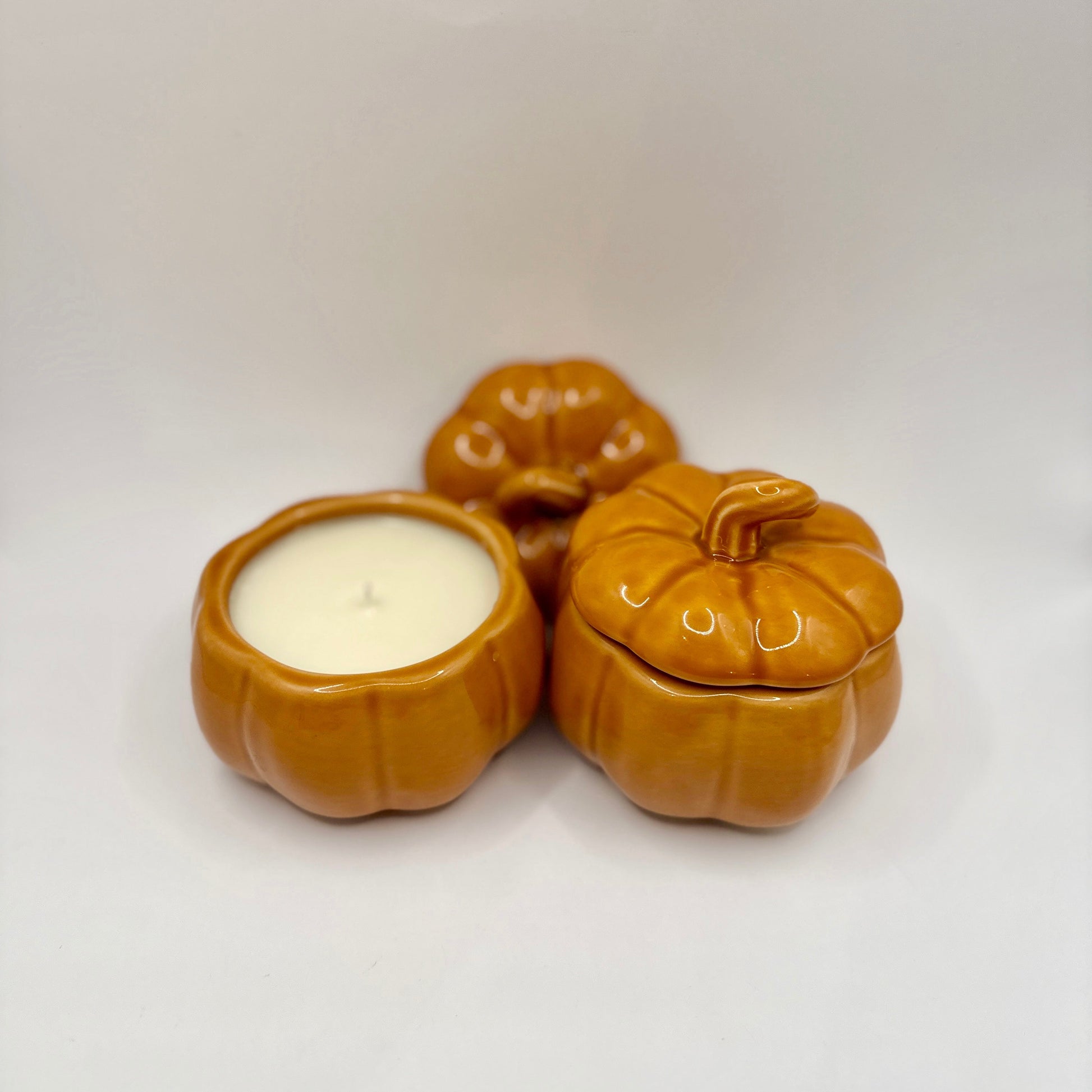 Three ceramic pumpkin-shaped containers with a candle on a white background
