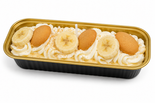 A banana cream cake in a black and gold plastic container, topped with piped whipped cream, banana slices, and vanilla wafers, on a white background.